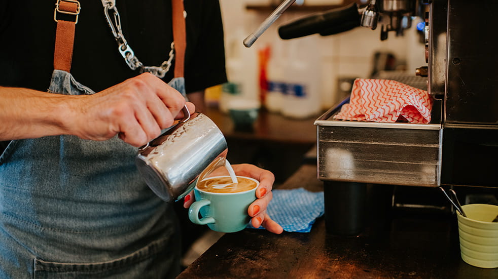 A close-up of a barista making a delicious latte coffee with milk.